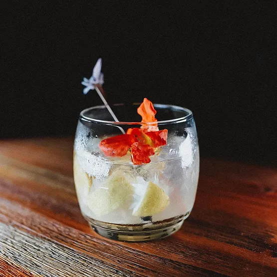 Verre de cocktail avec glaçons et garniture colorée sur une table en bois.