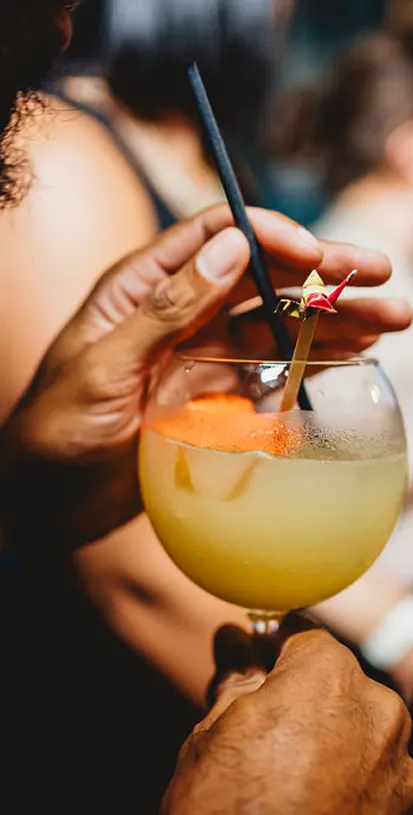 Main tenant un cocktail jaune avec une paille noire et une décoration.