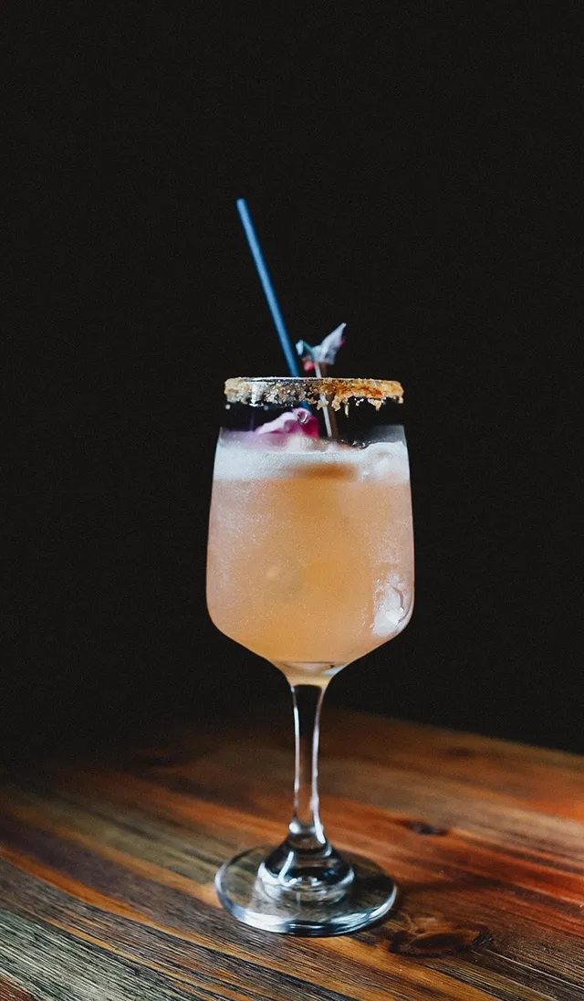 Verre à cocktail avec paille et tranche de citron sur fond sombre.