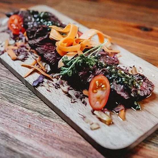 Tranches de viande avec légumes et herbes sur une planche en bois.