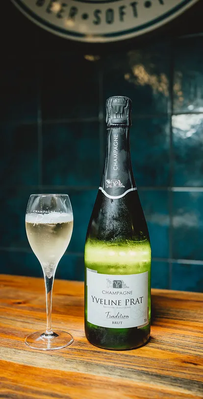 Bouteille et verre de champagne Yveline Prat sur table en bois.