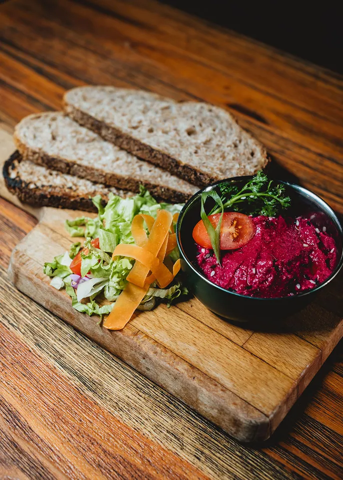 Salade, tartinade de betterave, pain sur planche en bois.