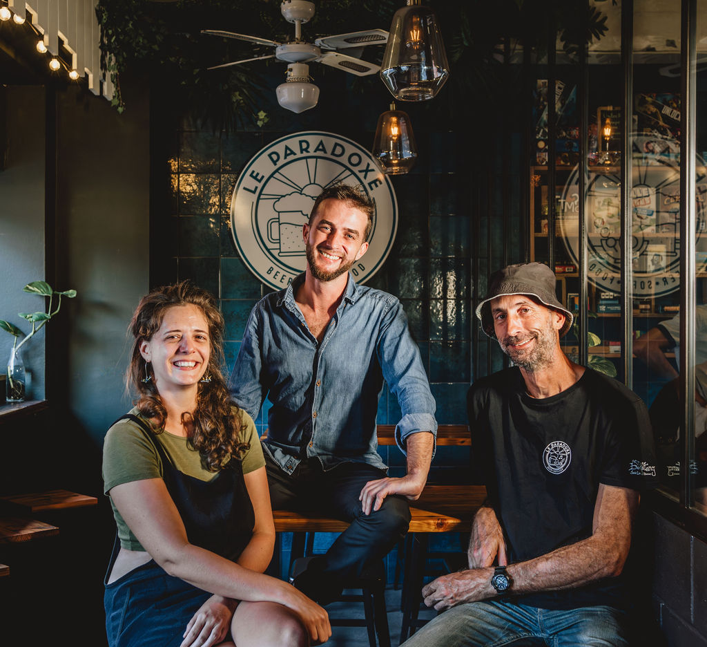 Trois personnes souriantes dans un café avec un logo "Le Paradoxe".