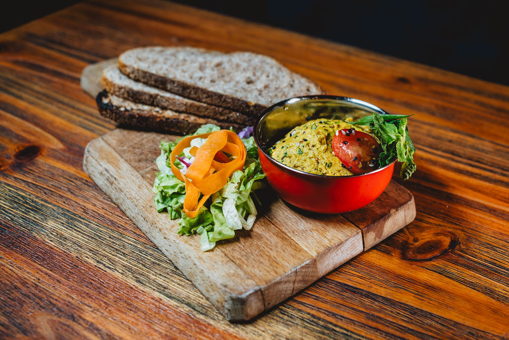Assiette avec pain, salade et bol de houmous sur une planche en bois.
