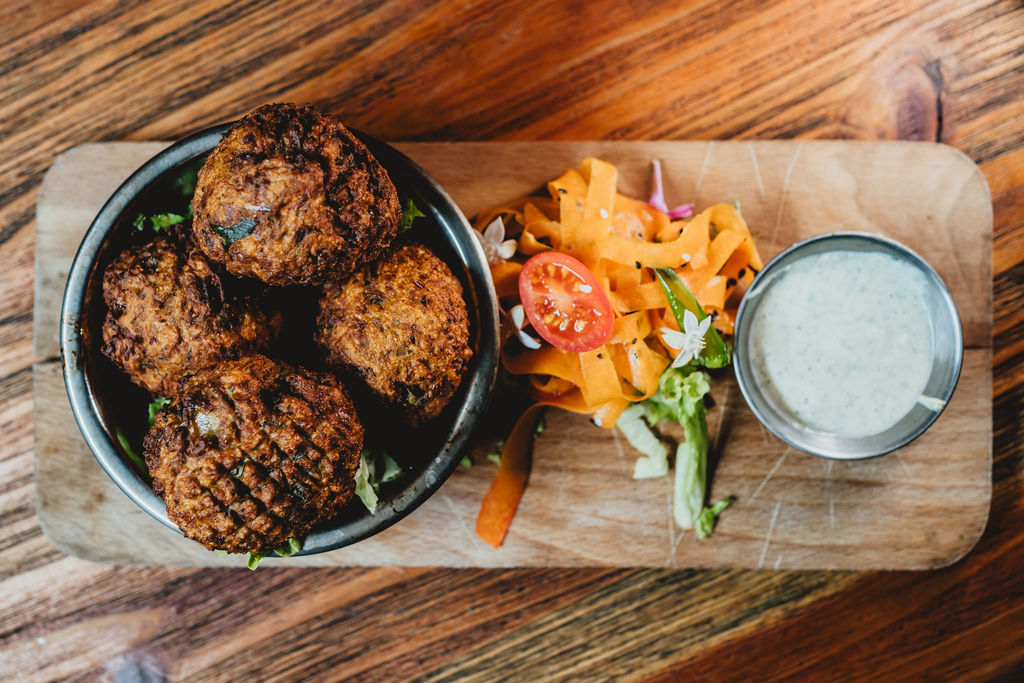 Boulettes frites avec salade et sauce blanche sur planche en bois.