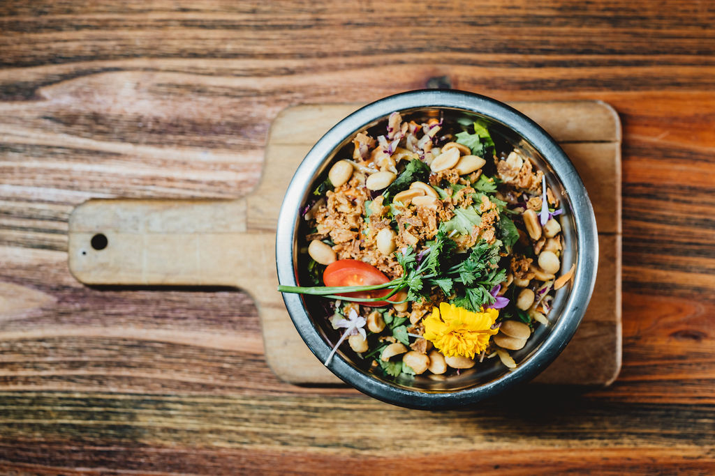 Salade colorée avec cacahuètes et fleurs comestibles dans un bol sur planche en bois.