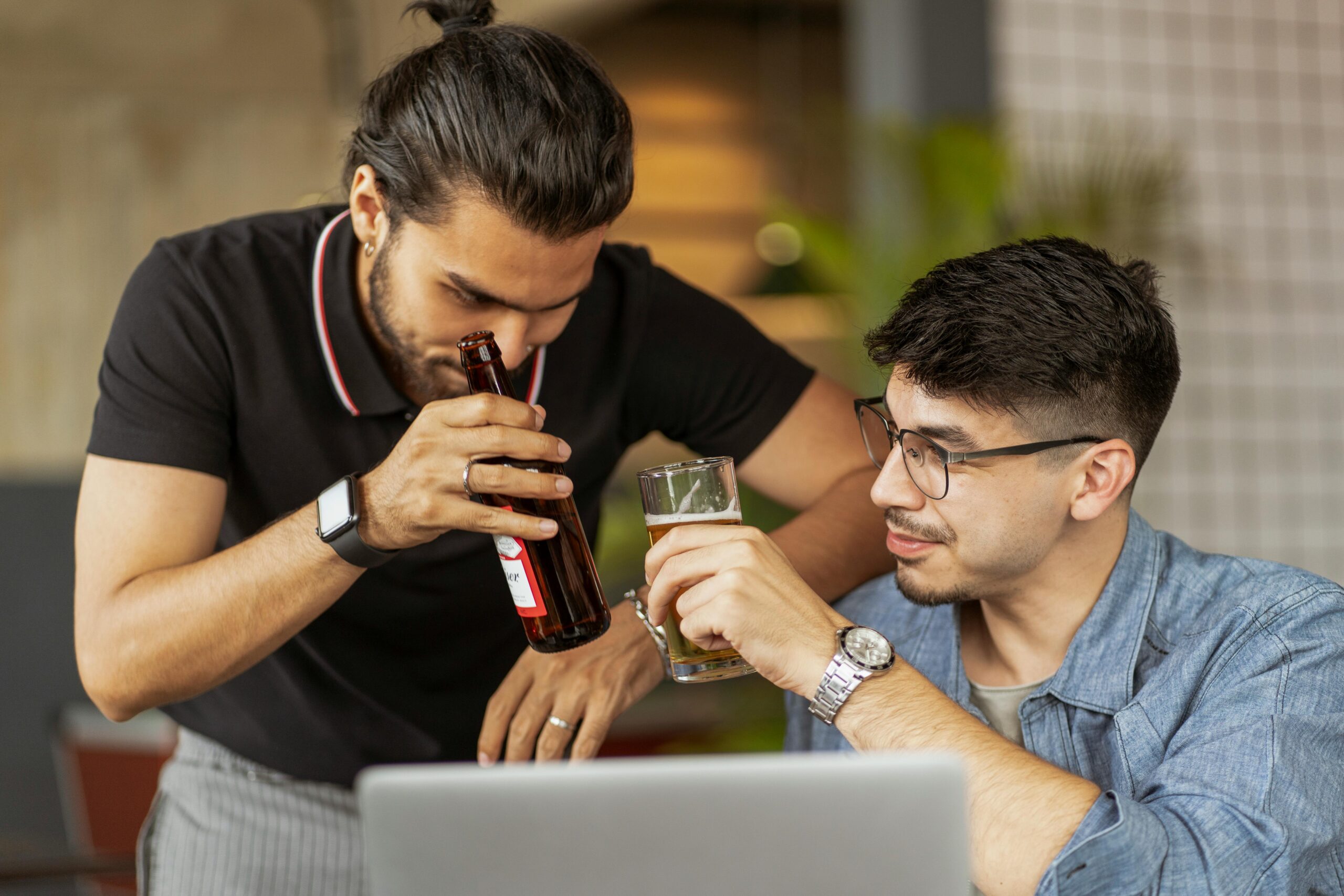 Deux hommes buvant de la bière devant un ordinateur portable.