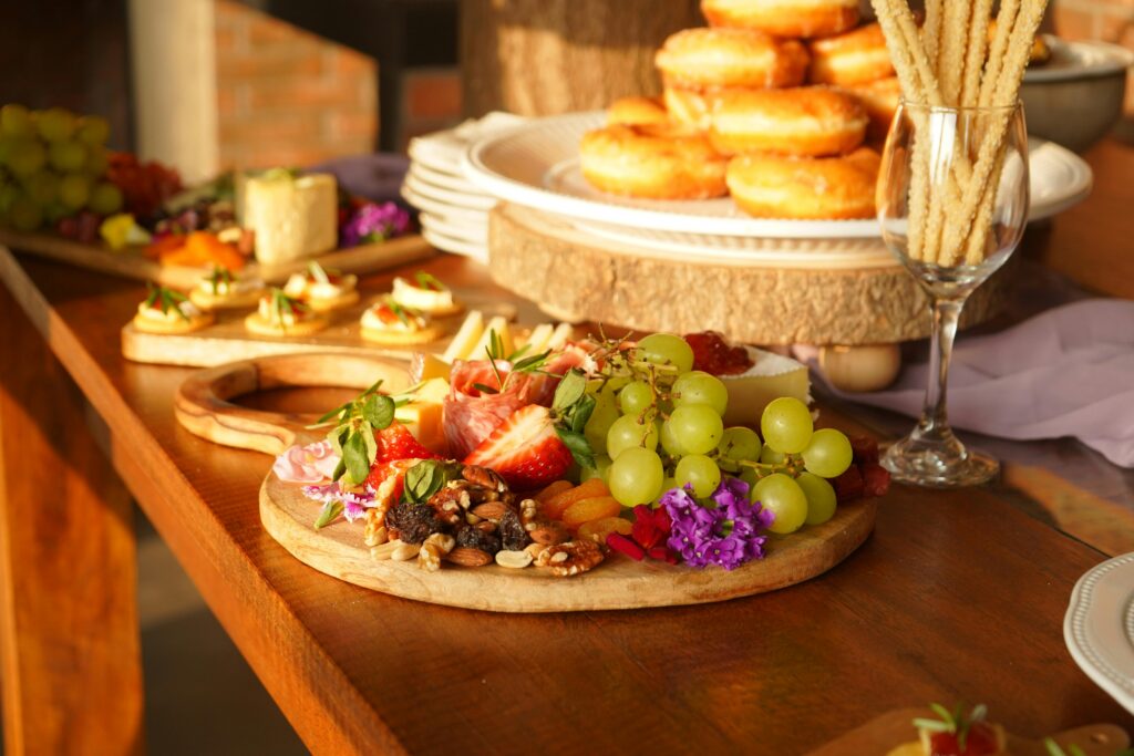 Plateau de charcuterie avec fruits, noix, fromage et pâtisseries sur une table en bois.